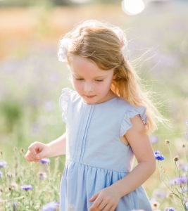 Young girl in blue top walking through the cornflowers in summer with her hair blowing in wind captured by Kika Mitchell Photography