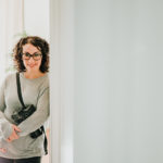 Chelmsford photographer Kika Mitchell Photography standing in doorway with camera on personal branding shoot at home