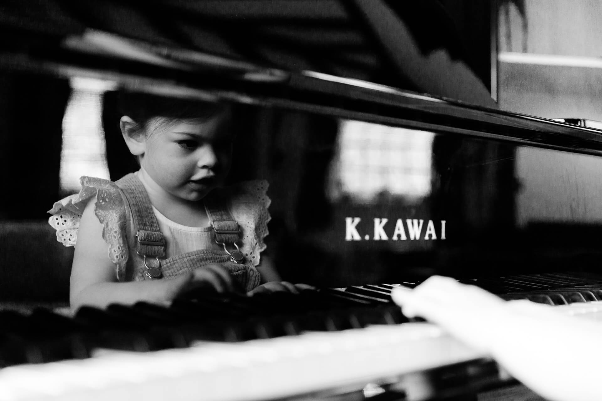 My style of monochrome image of little girl playing a grand piano in Black Notley captured by Chelmsford photographer Kika Mitchell Photography