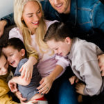 laughing family of 5 on sofa on Emily Norris's latest family shoot by Chelmsford photographer Kika Mitchell Photography