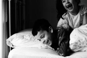 monochrome image of brother and sister in bed, gappy laughter captured by Chelmsford Photographer Kika Mitchell Photography
