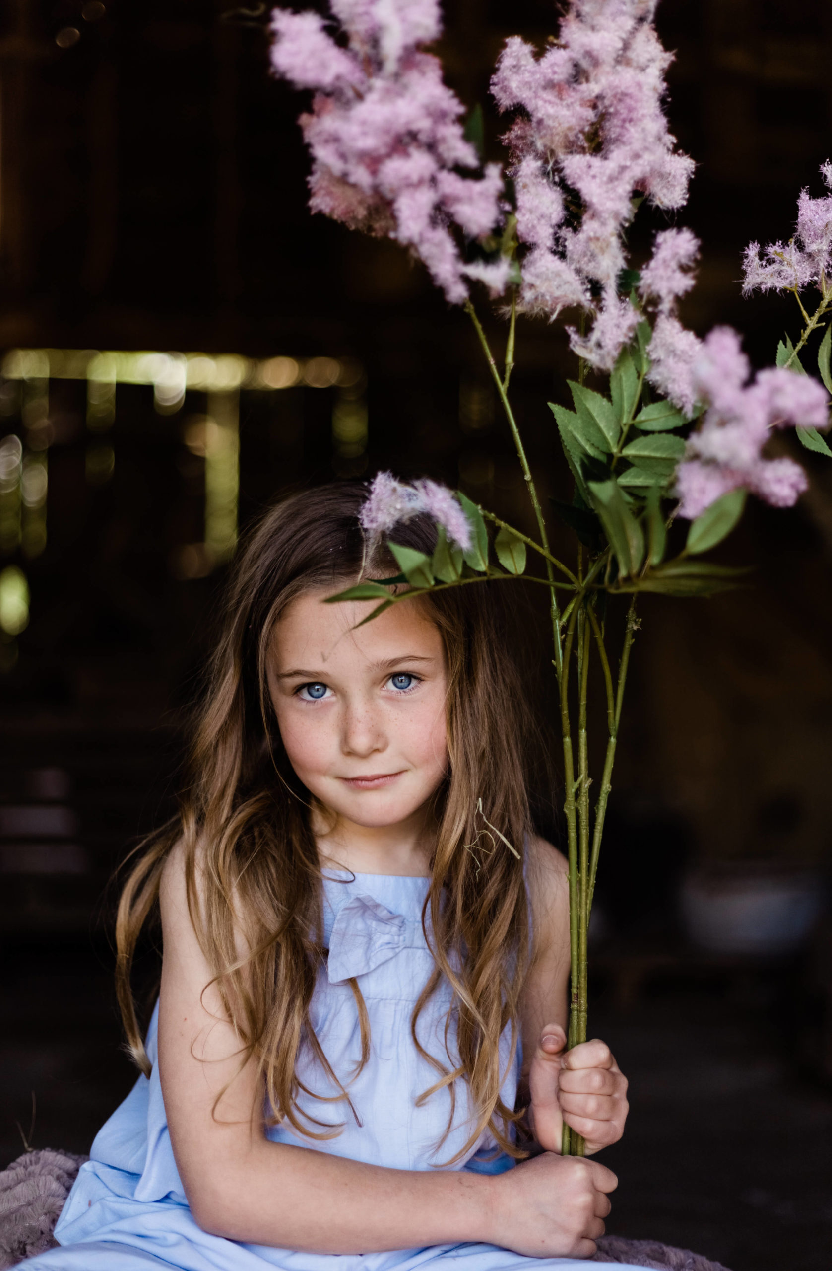 young girl in blue holds purple flowers whilst looking to camera captured by Chelmsford photographer Kika mItchell photography