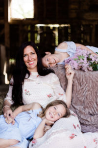 smiling mother and daughters, one on hay bale behind captured by Portrait of motherhood photographer Kika Mitchell Photography