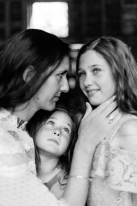 mother holds daughter's face as other daughter gazes at her sister in monochrome portrait of motherhood by Kika Mitchell photography Chelmsford photographer