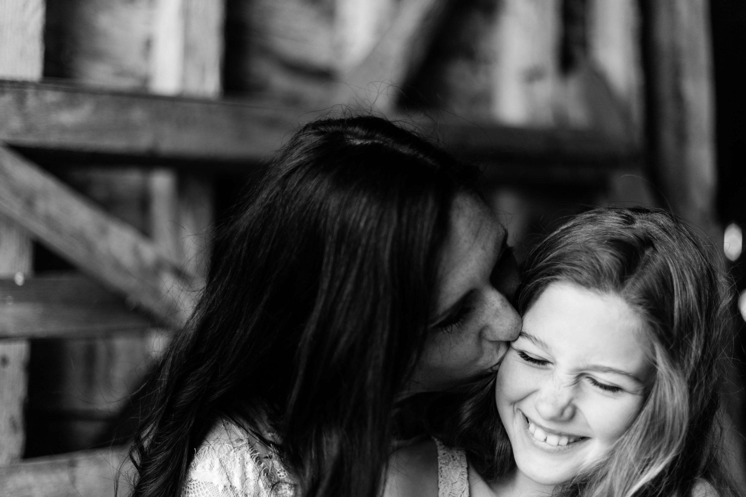 black and white image of mother and daughter, daughter crinkles nose as mother kisses her by chelmsford photographer Kika mitchell photography