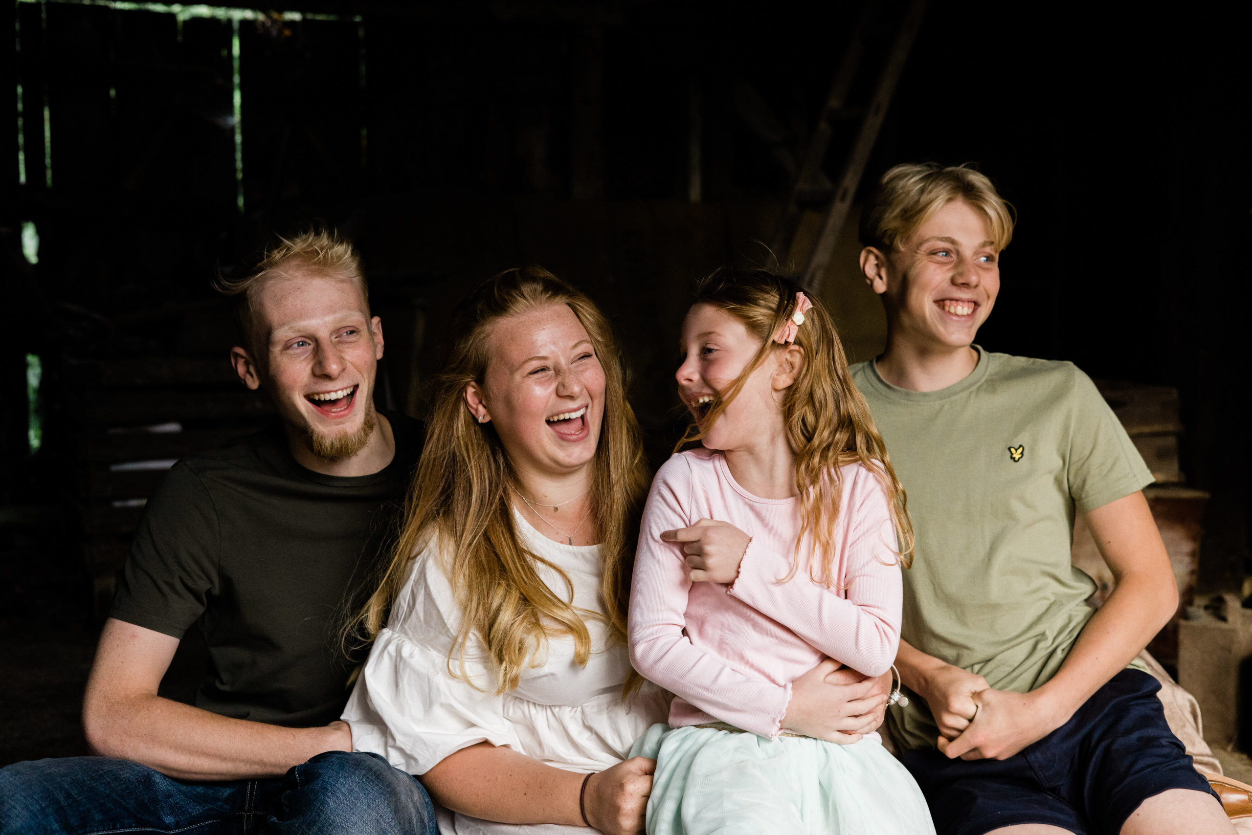 4 laughing siblings in barn captured by family photographer chelmsford Kika mitchell photography