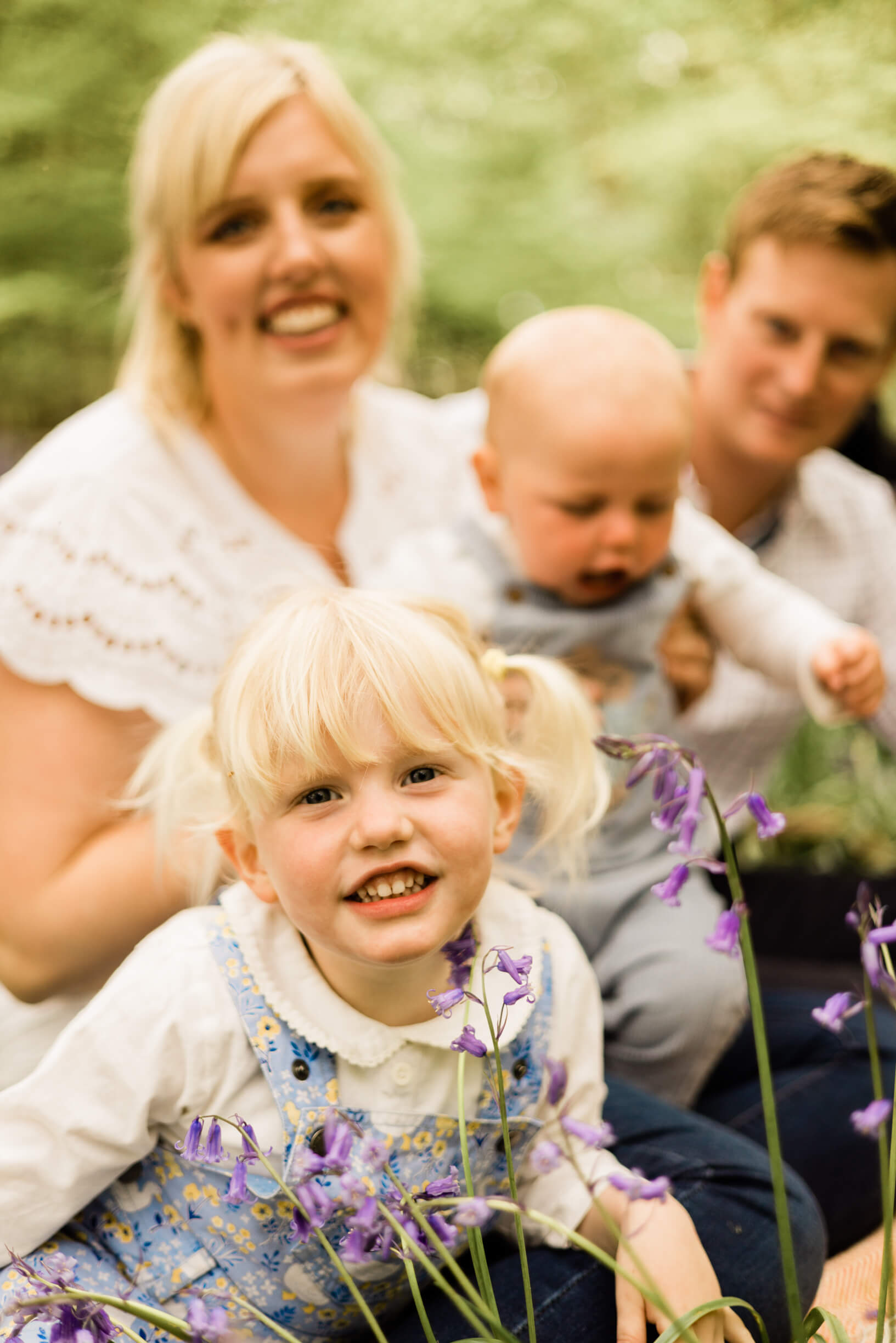 Smiling girl with baby sibling and parents during their relaxed family Bluebell shoot by Chelmsford photographer Kika Mitchell Photography