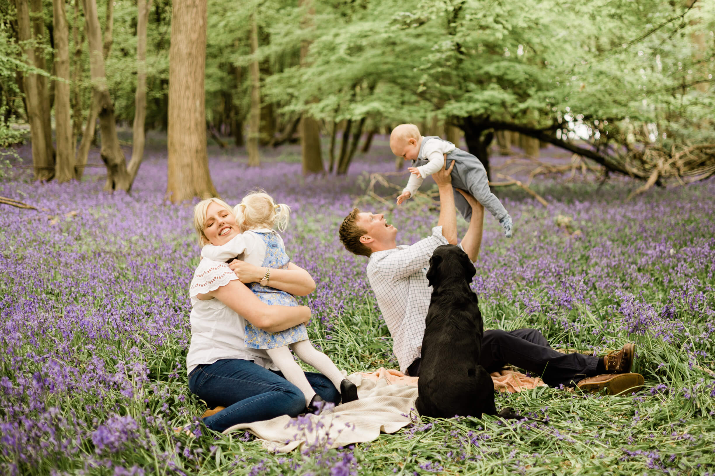 Beaming, relaxed family during their woodland bluebell photo shoot captured by Chelmsford photographer - Kika Mitchell Photography