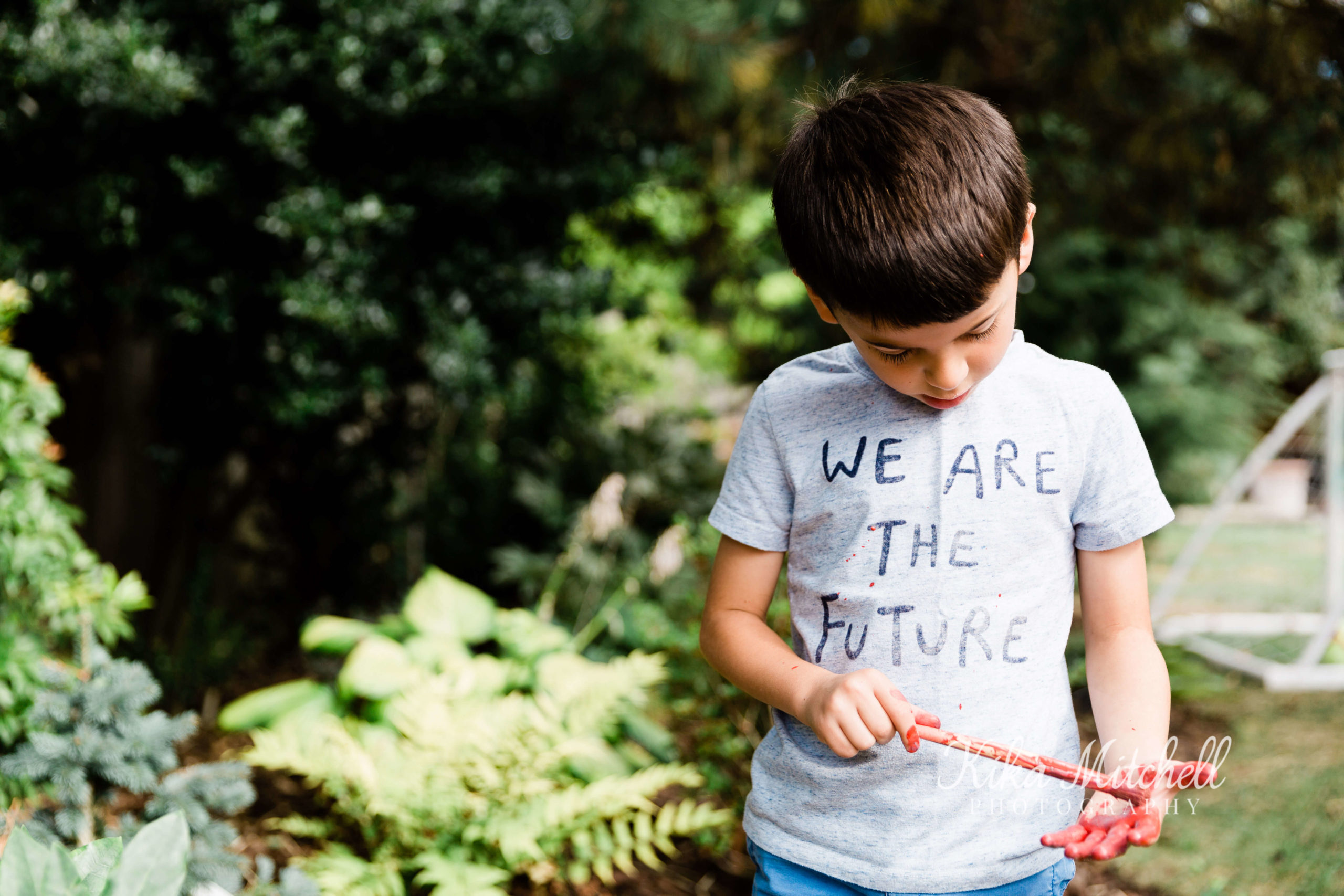 male child walking through woodland, holding a stick - t shirt reads 'we are the future'