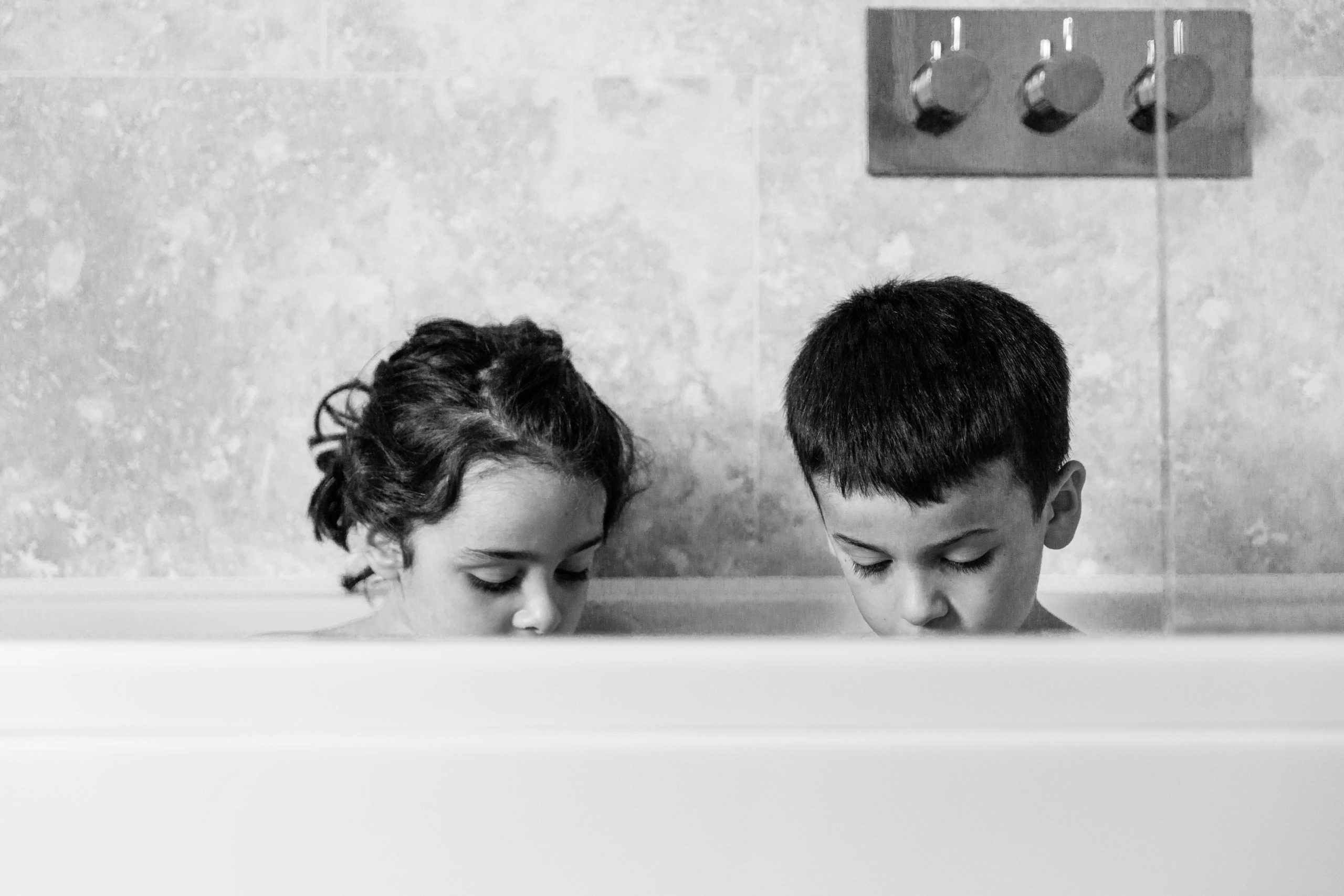 black and white style photo of two children's heads which are just visible about the bath